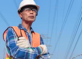 Low angle portrait of a senior Asian electrician wearing a helmet and safety glasses holding a radio transmitter.
