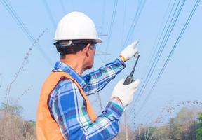 Behind the senior Asian electrician wearing a white helmet and holding a radio transmitter. photo