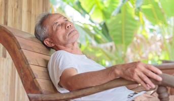 Depressed senior man sits on a rocking chair and thinks. Disappointed retired man sitting in a chair A melancholy old man sat alone at the nursing home with a sad expression on his face. photo