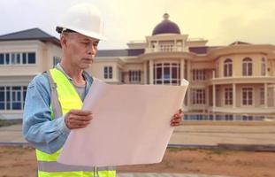 Middle-aged construction engineer in hard hat with project in hand. Asian elders standing in construction site photo