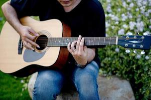 foto de un guitarrista, un joven tocando una guitarra mientras se sienta en un jardín natural, concepto musical