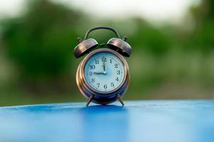 Golden alarm clock picture placed on a blue table, green background Punctual concept With copy space photo