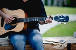 Picture of a guitarist, a young man playing a guitar while sitting in a natural garden,music concept photo