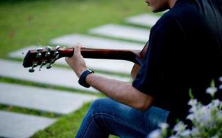 Picture of a guitarist, a young man playing a guitar while sitting in a natural garden,music concept photo