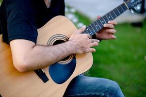 Picture of a guitarist, a young man playing a guitar while sitting in a natural garden,music concept photo