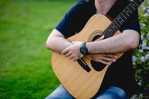 Picture of a guitarist, a young man playing a guitar while sitting in a natural garden,music concept photo