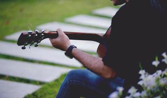 Picture of a guitarist, a young man playing a guitar while sitting in a natural garden,music concept photo