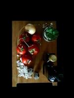 Some fresh red tomatoes and a golden onion placed on a wooden cutting board next to two bottles of oil and a few white salt crystals photo