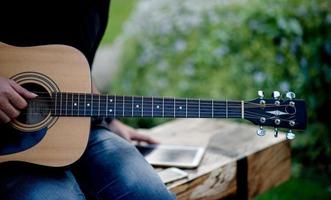 Picture of a guitarist, a young man playing a guitar while sitting in a natural garden,music concept photo