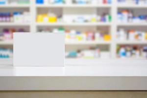 Blank white medicine package on counter with blur shelves of drug in the pharmacy drugstore photo