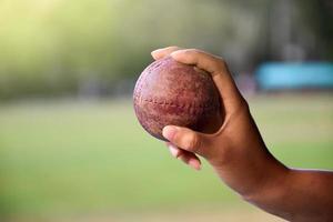 pelota de cricket para practicar o entrenar en la mano, fondo de cancha de césped verde borroso, concepto para los amantes del deporte de cricket en todo el mundo. foto