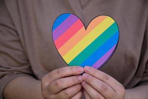 Two hearts made of rainbow colored paper are holding in hands of the LGBT person, concept for lgbtq communities celebrations in pride month around the world photo