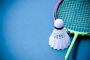 volante de bádminton blanco crema y raqueta con sombreado de luz de neón en el suelo verde en la cancha de bádminton cubierta, fondo de bádminton borroso, espacio para copiar. foto