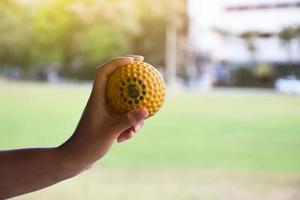 pelota de cricket para practicar o entrenar en la mano, fondo de cancha de césped verde borroso, concepto para los amantes del deporte de cricket en todo el mundo. foto