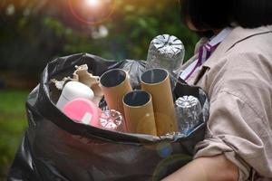 el propietario lleva una bolsa de plástico negra llena de basura, botellas de plástico, cartones, botellas de leche y papel usado para separar y manejar la basura en el hogar. enfoque suave y selectivo en la basura. foto