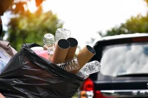 el propietario lleva una bolsa de plástico negra llena de basura, botellas de plástico, cartones, botellas de leche y papel usado para separar y manejar la basura en el hogar. enfoque suave y selectivo en la basura. foto