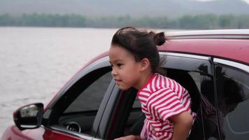 schattige aziatische broers en zussen meisjes glimlachen en hebben plezier met het reizen met de auto en kijken uit het autoraam. gelukkige familie genieten van road trip op zomervakantie. video