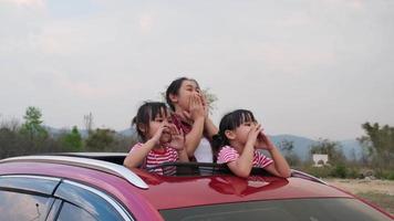 familia feliz disfrutando de un viaje por carretera en vacaciones de verano. madre e hijo disfrutando de la naturaleza en el camino en el coche en el techo corredizo. concepto familiar de vacaciones y viajes. video