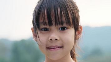 mignon enfant d'âge préscolaire asiatique souriant joyeusement faisant des mains en forme de coeur sur les yeux sur fond de nature verdoyante. video