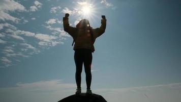 silueta de una exitosa excursionista con los brazos abiertos en la cima de una montaña. mujer feliz de pie con los brazos levantados en el fondo de la puesta de sol entre las montañas video