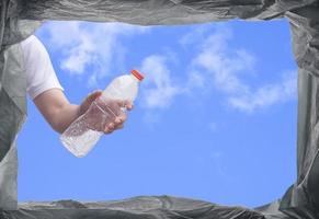 View from below of young man hand throwing plastic water bottle into trash bin in public area photo