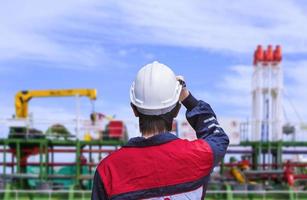 Rear view of young engineer in blue mechanic jumpsuit wearing white safety helmet before working on oil tanker ship at shipyard photo