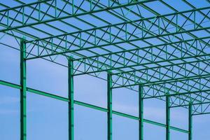 Low angle view of green steel roof of warehouse building structure in construction area against blue sky background photo
