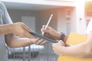 Close up female hand using electronic pen to signing signature on tablet after received parcel box from delivery man in front of home photo