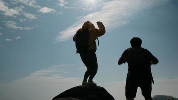silueta de una exitosa pareja asiática levantando los brazos en la cima de una montaña disfrutando de la vista del valle antes del atardecer. video