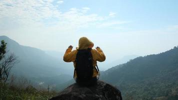 Successful woman hiker open arms on top of a mountain. Happy woman sitting on a rock raising her hands on the background of the sunrise between the mountains