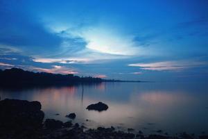 Amazing seascape in a sumatera beach. Beach with rocks beside it. Shoot with slow shutter speed or soft focus. Reflection of forest beside the beach under the blue sky. photo