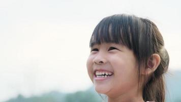 retrato de un lindo preescolar asiático sonriendo alegremente en el jardín de verano. niña asiática que muestra los dientes delanteros con una gran sonrisa en el fondo verde de la naturaleza.