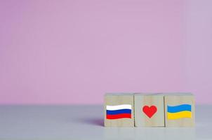 Wooden cubes with russia flag symbol and ukraine flag with red heart icon on background. photo
