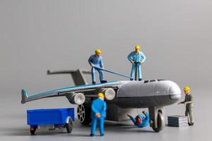 equipo de trabajadores en miniatura revisando y reparando aviones sobre fondo gris foto