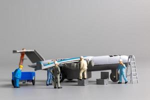 Miniature worker team checking and repairing airplane on gray background photo