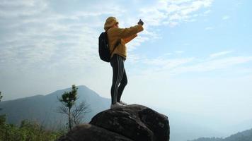 Female hiker standing on top of a mountain at sunrise and using a smartphone. video