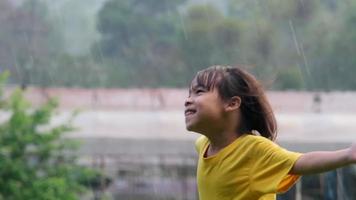 Cute little girl having fun catching rain drops. Kids play in summer rain. Child playing outdoor on rainy day. video