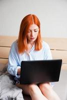 young work from home woman sitting on bed with laptop computer photo