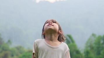 bambina sveglia che si diverte a catturare le gocce di pioggia. i bambini giocano sotto la pioggia estiva. bambino che gioca all'aperto in una giornata piovosa. video