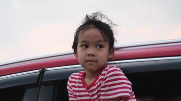 linda niña asiática sonriendo y divirtiéndose para viajar en auto y mirando por la ventana del auto. familia feliz disfrutando de un viaje por carretera en vacaciones de verano. video