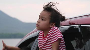 menina asiática bonitinha sorrindo e se divertindo para viajar de carro e olhando pela janela do carro. família feliz aproveitando a viagem nas férias de verão.