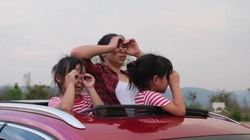 familia feliz disfrutando de un viaje por carretera en vacaciones de verano. madre e hijo disfrutando de la naturaleza en el camino en el coche en el techo corredizo. concepto familiar de vacaciones y viajes. video