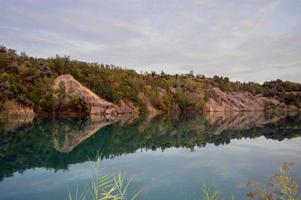 landscape on the water with a steep bank overgrown with trees and shrubs photo