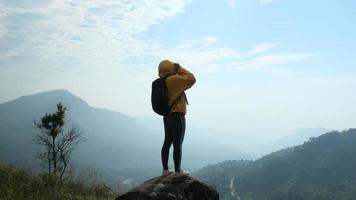 excursionista femenina de pie sobre rocas en el fondo del amanecer entre montañas. las excursionistas exitosas disfrutan de la naturaleza en la cima de la montaña. video