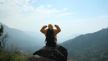 randonneur femme réussie bras ouverts au sommet d'une montagne. femme heureuse assise sur un rocher levant les mains sur le fond du lever du soleil entre les montagnes video