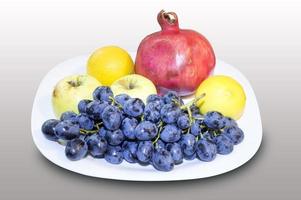 pomegranate, grape with apple and lemon in a white plate photo