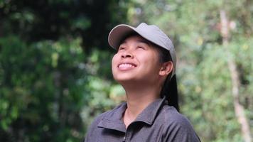 Tired Asian female athlete in sports uniform resting after jogging in a green park on a sunny day. Fitness and lifestyle concept. video