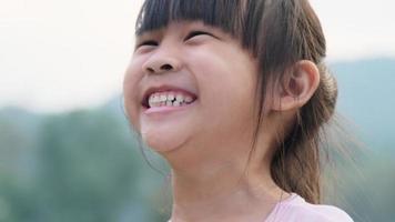 retrato de un lindo preescolar asiático sonriendo alegremente en el jardín de verano. niña asiática que muestra los dientes delanteros con una gran sonrisa en el fondo verde de la naturaleza.