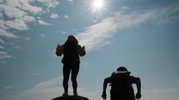 silhueta de um casal asiático bem sucedido, levantando os braços no topo de uma montanha, apreciando a vista do vale antes do pôr do sol. video