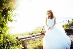 bride with a bouquet of flowers near the water photo